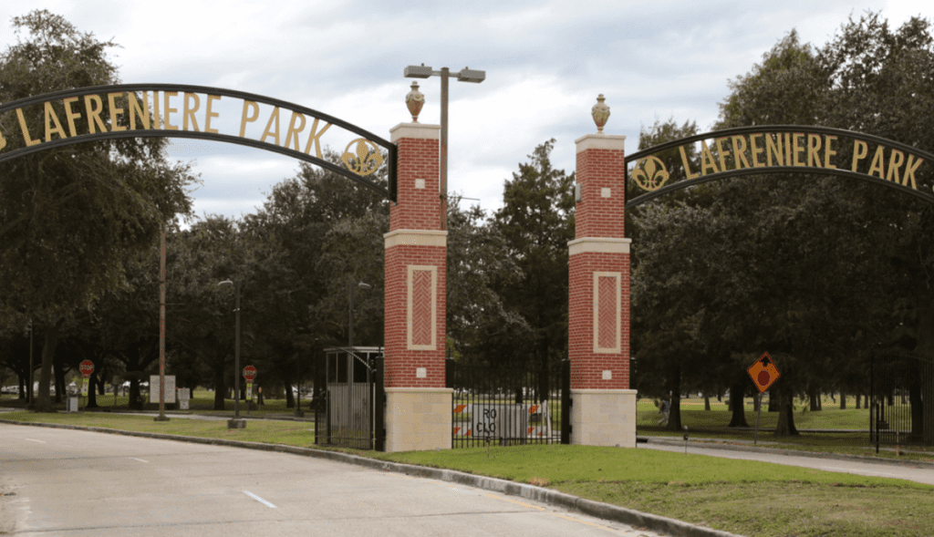 The entrance gates to Lafreniere Park in Metairie, Louisiana. Beyond the open gates are grassy fields and tall trees, with people walking around.