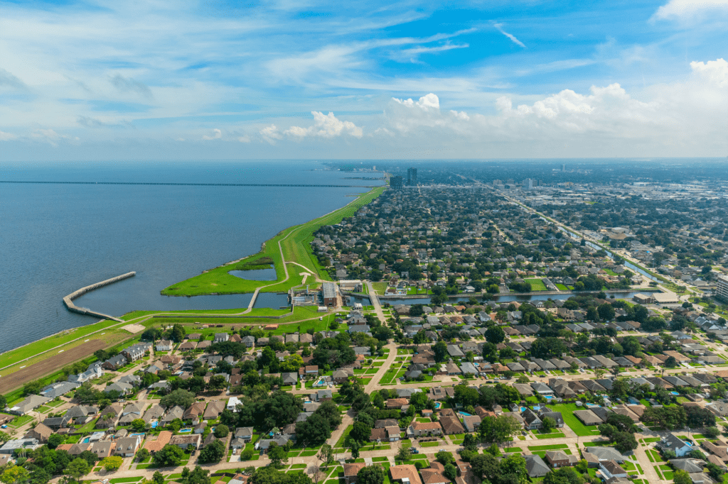 Metairie seen from a bird's-eye view. It is bright green and full of trees and pretty houses, with a bright blue ocean to the left.